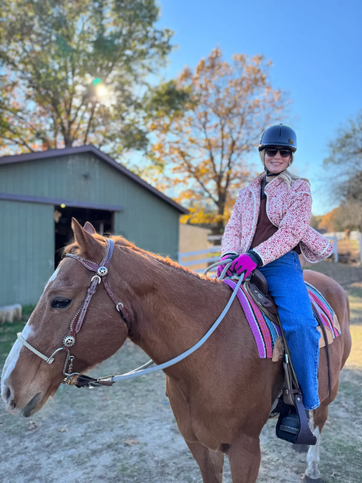Rider on chestnut horse by barn with autumn foliage and golden light