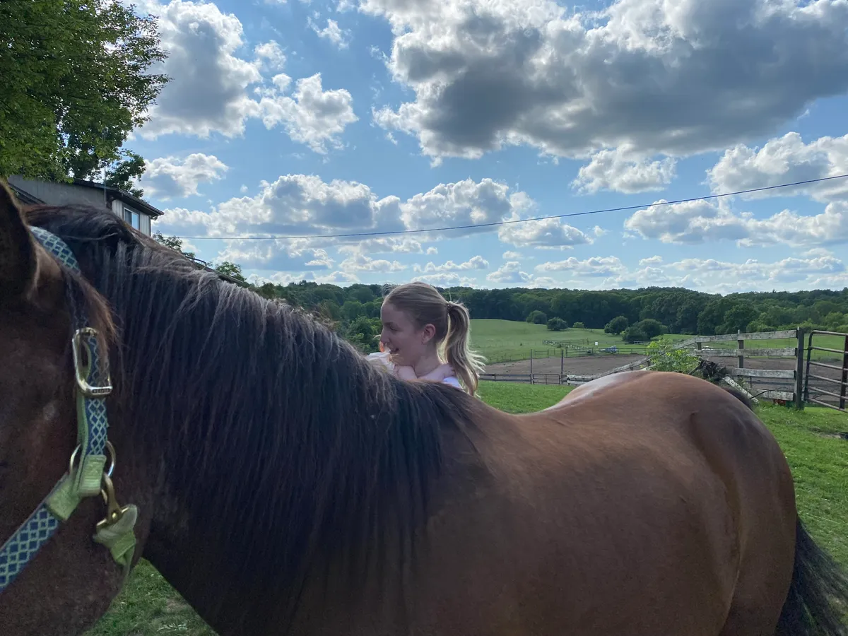 Person embracing a horse with a wide open pasture behind them